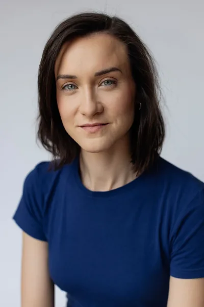 Magdalena Tarnawska-Stus - headshot na jasnoniebieskim tle, lekki uśmiech, ramię 3/4