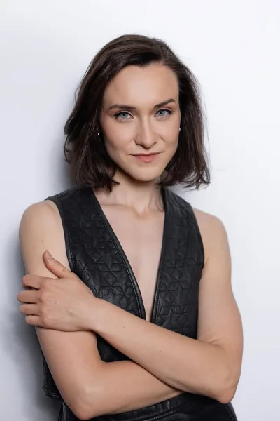 Magdalena Tarnawska-Stus - portret w beżowym kombinezonie, zielona kurtyna w tle